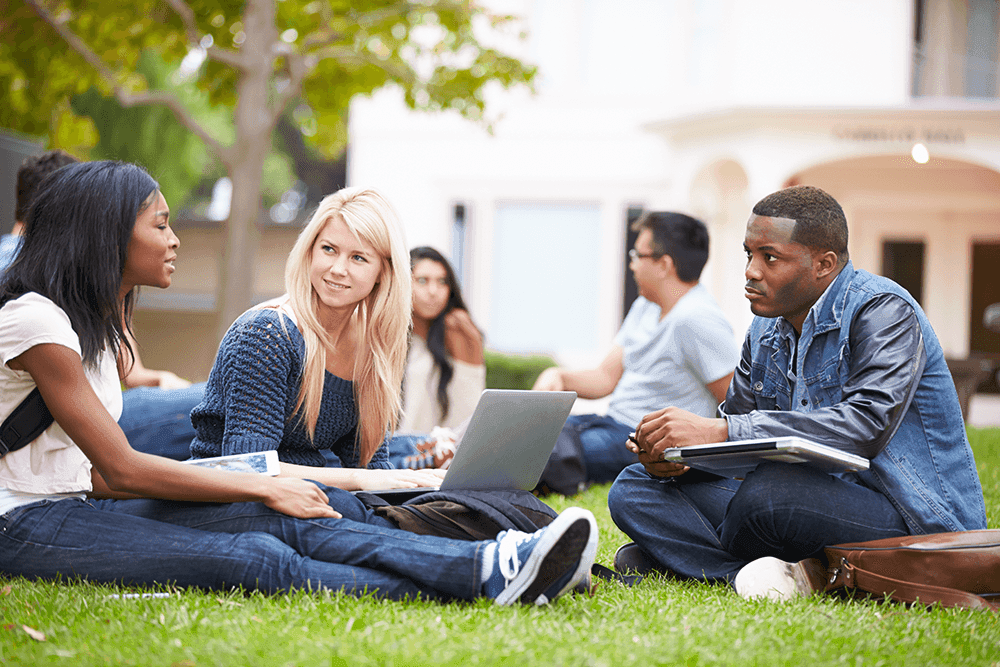 students sitting outside on campus sitting on grass
