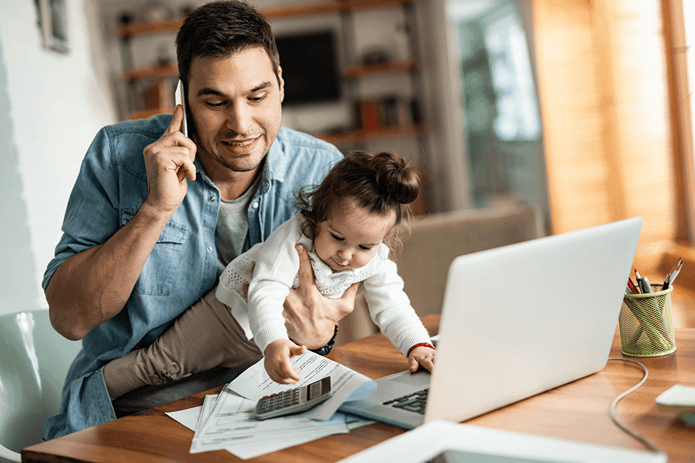 Image of a man sitting at a laptop with a baby on his lap